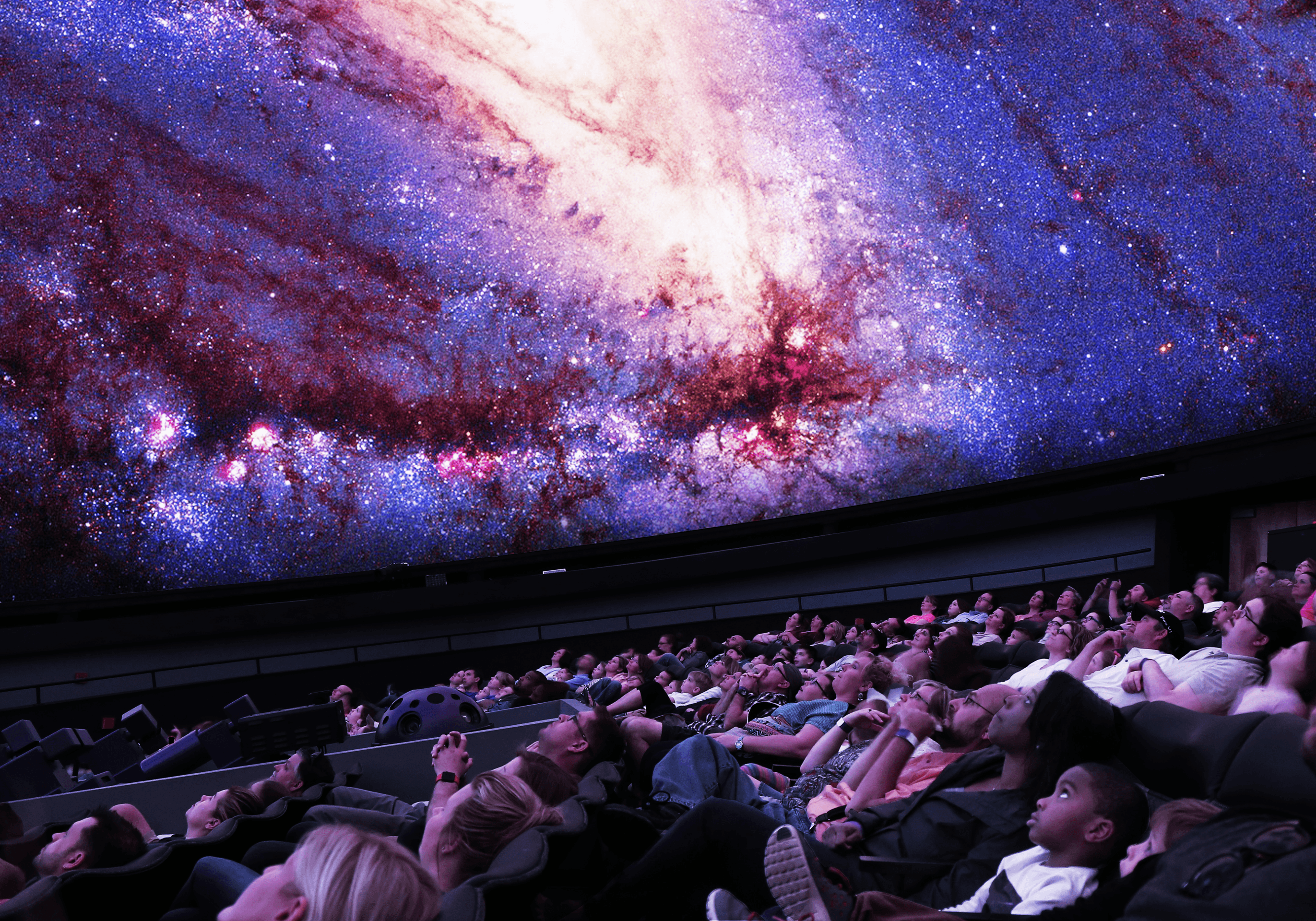 People watching a colorful galaxy projection inside a planetarium.
